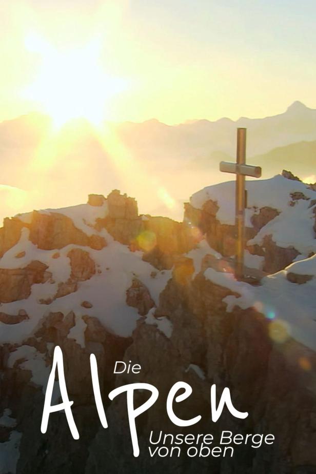 Ein Gipfelkreuz auf einem schneebedeckten Berg in den Alpen bei Sonnenaufgang.
