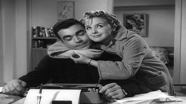 Eine Frau umarmt einen Mann, der an einer Schreibmaschine sitzt.