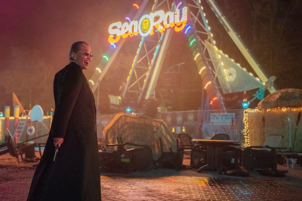 Sharon Stone steht in „Nobody 2“ böse lachend mit Waffe in der Hand vor einem Vergnügungspark.