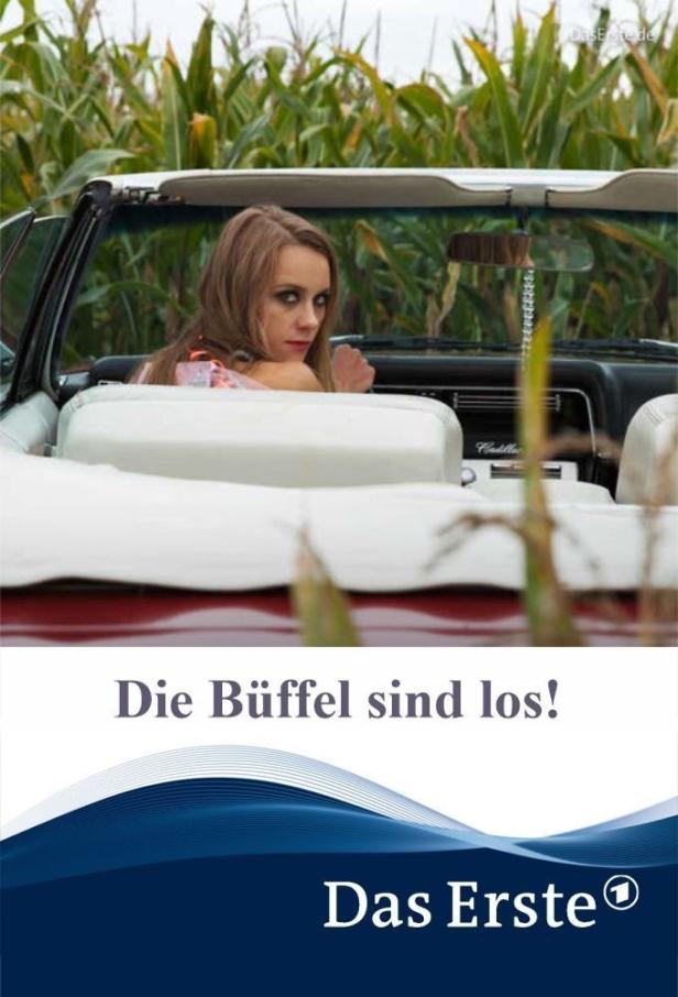 Eine Frau sitzt in einem roten Cadillac Cabrio vor einem Maisfeld.