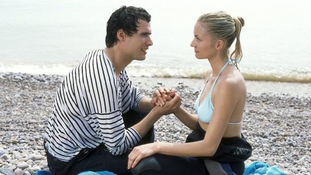Ein Paar sitzt am Strand und hält Händchen.