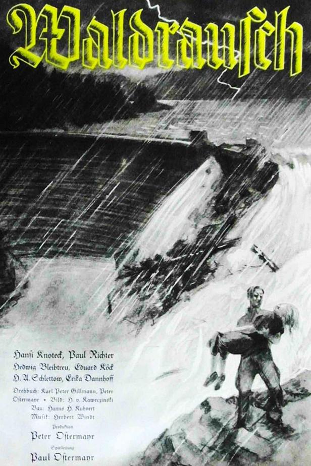 Ein Mann trägt eine bewusstlose Frau in einem Sturm, Szene aus dem Film „Waldrausch“.