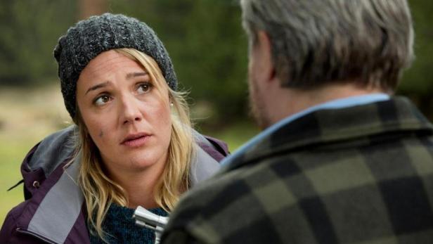 Eine Frau mit Mütze und besorgtem Blick hält eine Waffe in der Hand.