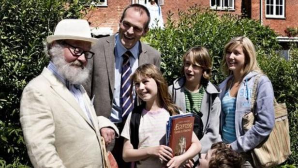 Eine Gruppe von Menschen steht vor einem Backsteingebäude und einem grünen Busch.