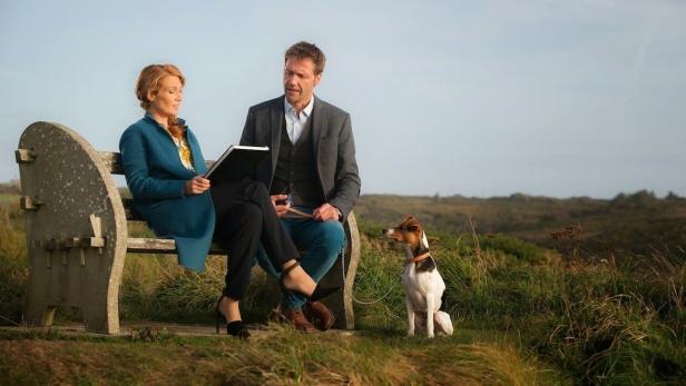 Ein Paar sitzt mit einem Hund auf einer Bank in der Natur.