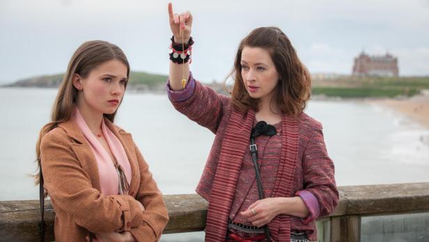 Zwei Frauen stehen an einer Küste, eine hält ein Pendel in der Hand.