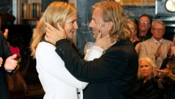 Ein Mann und eine Frau umarmen sich vor einer applaudierenden Menschenmenge.