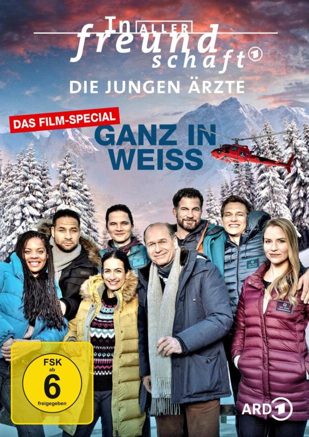 Das Filmplakat zu „In aller Freundschaft – Die jungen Ärzte: Ganz in Weiss“ mit dem Ensemble vor verschneiter Bergkulisse.