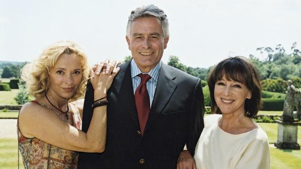 Ein Mann in Anzug posiert mit zwei Frauen im Freien.