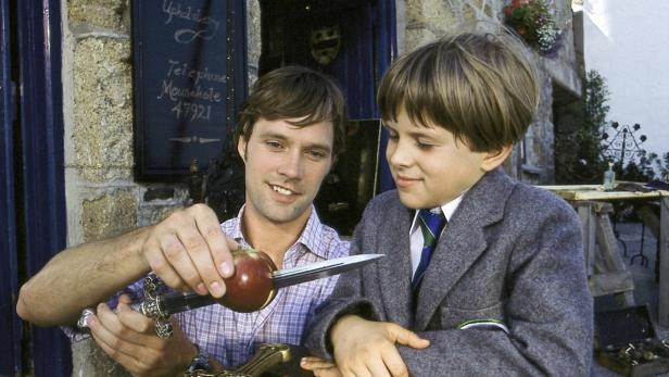 Ein Mann zeigt einem Jungen, wie man einen Apfel mit einem Dolch aufspießt.