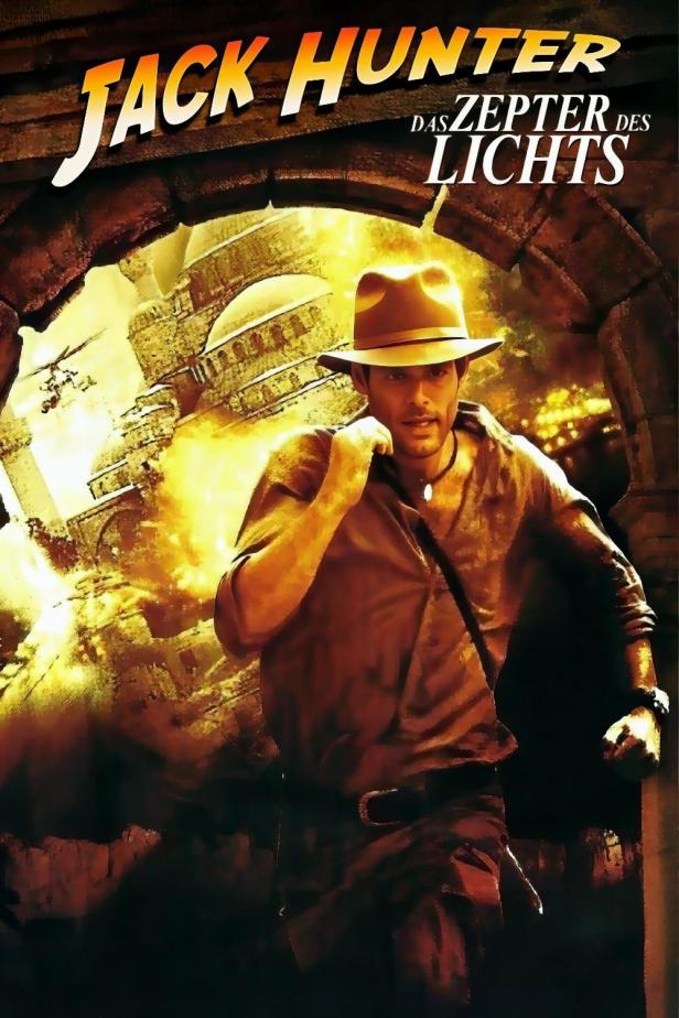 Ein Mann im Fedora-Hut vor dem Hintergrund des Filmposters „Jack Hunter und das Zepter des Lichts“.