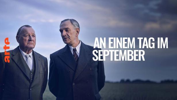 Zwei Männer in Anzügen vor dem Hintergrund des Filmtitels „An einem Tag im September“.