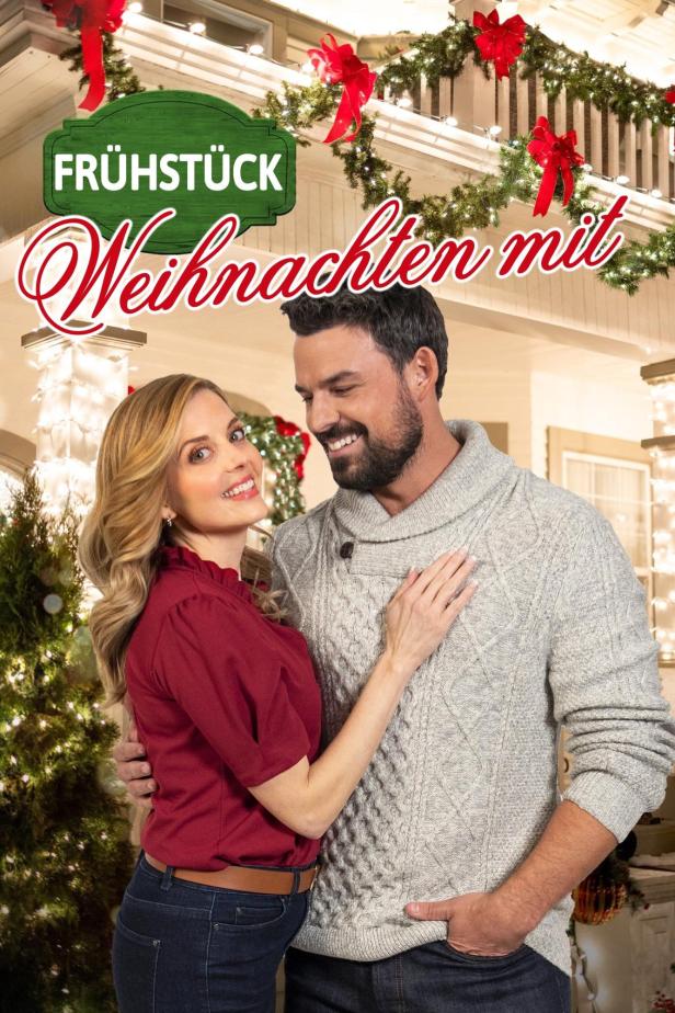 Ein lächelndes Paar umarmt sich vor einem weihnachtlich geschmückten Haus.