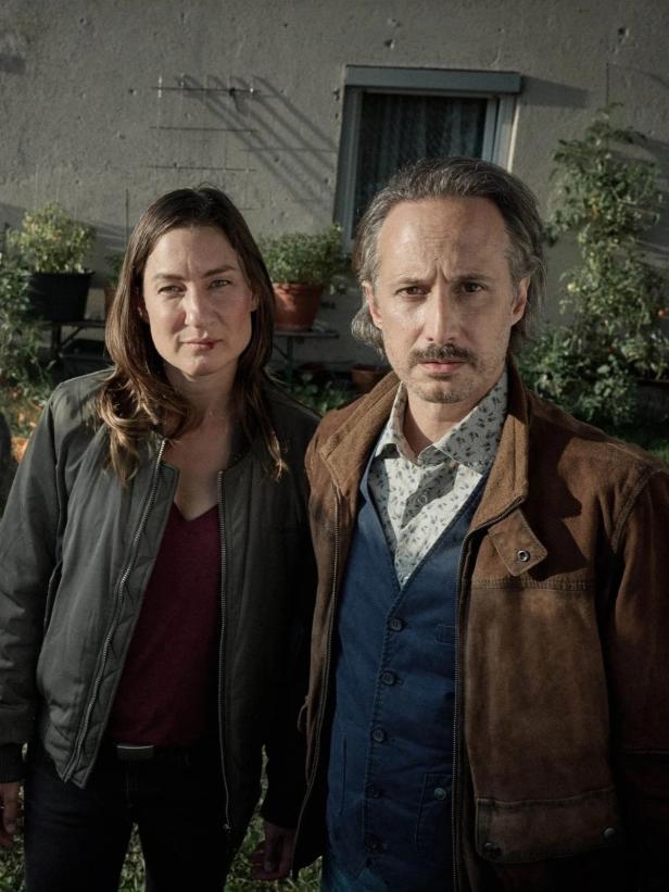 Eine Frau und ein Mann stehen vor einer Hauswand mit Pflanzenkübeln.