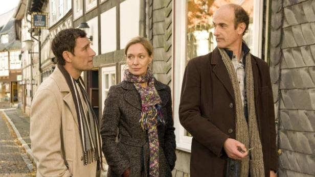 Drei Personen stehen vor einem Fachwerkhaus und unterhalten sich.