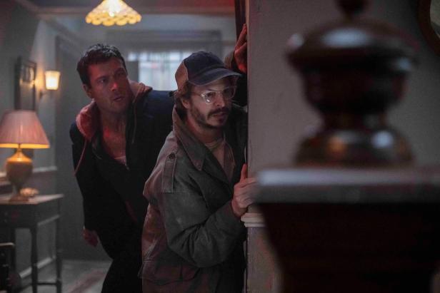 Zwei Männer blicken vorsichtig um die Ecke eines Hausflurs