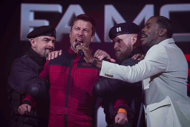 Mann in rotem Dress wird von zwei Uniformierten festgehalten, während er in ein Mikro brüllt