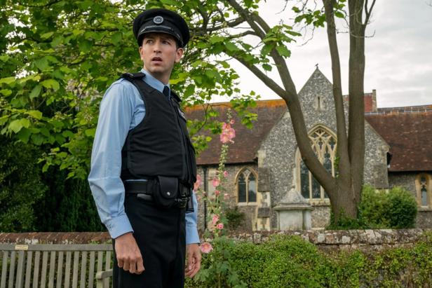 Polizist steht auf englischem orfplatz vor der Kirche