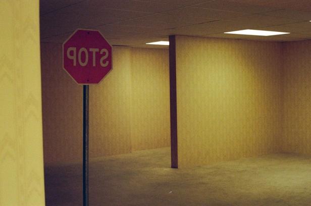 Ein umgedrehtes Stoppschild steht in einem leeren, gelb beleuchteten Raum mit Teppichboden und Trennwänden.
