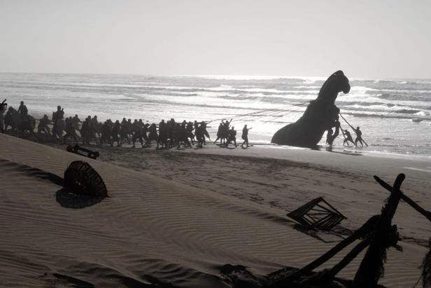 Menschen ziehen das riesige trojanische Pferd von einem Strand am Meer weg.