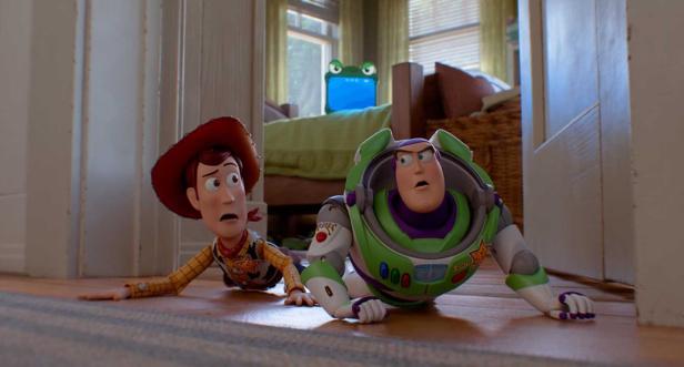 Woody und Buzz kriechen erschrocken durch einen Flur, während im Hintergrund ein Tablet mit Augen auf einem Bett steht.