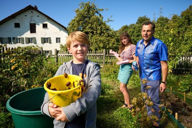 Ein Junge hält einen Eimer mit gesammelten Schnecken im Garten, dahinter stehen zwei Erwachsene.