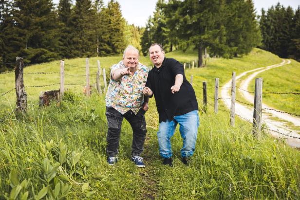 Zwei Männer stehen auf einem Feldweg neben einem Weidezaun und zeigen gemeinsam in Richtung der Kamera.