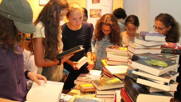 Mehrere Jugendliche stehen an einem Tisch voller Bücher und lesen.