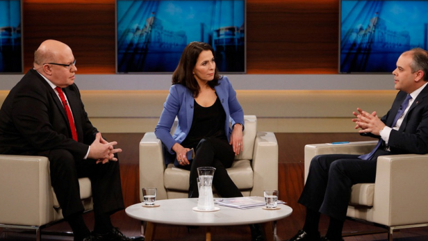 Drei Personen sitzen in Sesseln in einem Fernsehstudio und diskutieren.