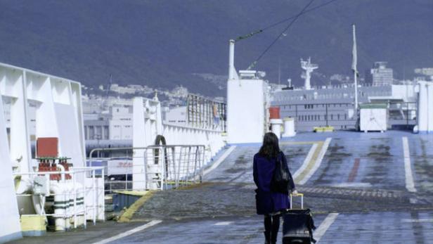 Eine Frau geht mit einem Rollkoffer auf dem Deck einer Fähre.