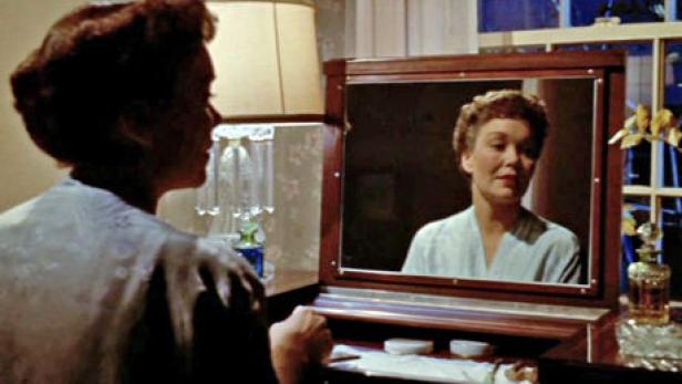 Eine Frau betrachtet ihr Spiegelbild an einem Schminktisch.