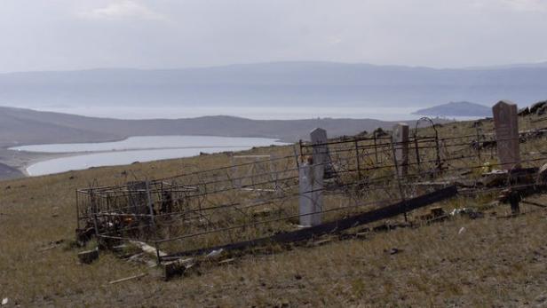 Ein Friedhof auf einem Hügel mit Blick auf einen See und Berge im Hintergrund.