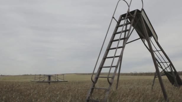 Eine verlassene Rutsche und ein Karussell stehen auf einem Feld mit hohem Gras.