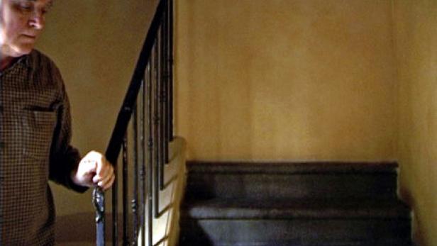 Ein älterer Mann geht eine Treppe hinauf und hält sich am Geländer fest.