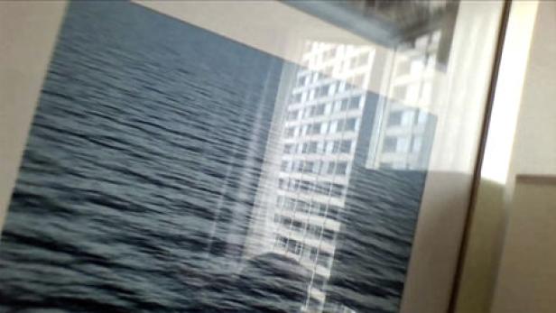 Ein Foto zeigt eine Meeresoberfläche mit der Spiegelung eines Gebäudes.