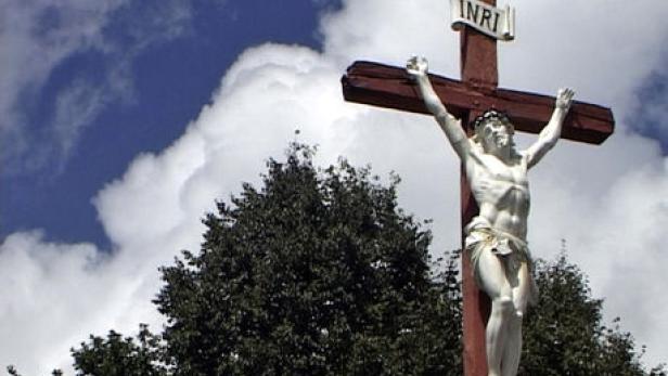 Eine Christusstatue an einem Holzkreuz unter blauem Himmel mit Wolken.