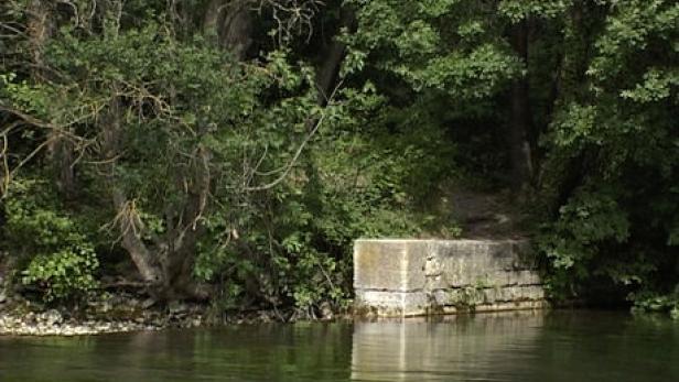 Ein Betonblock steht am Ufer eines Flusses, umgeben von Bäumen.