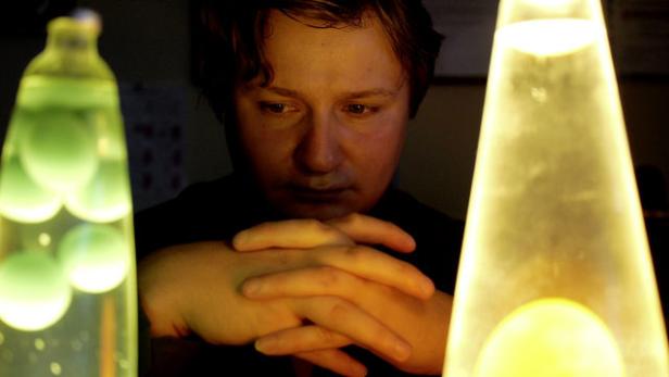 Ein Mann sitzt zwischen zwei Lavaleuchten und blickt nachdenklich nach unten.