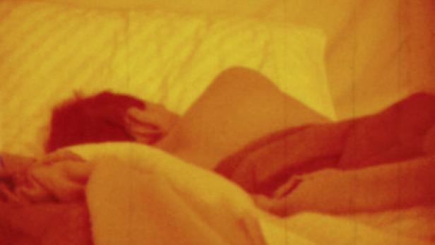 Eine Person liegt in einem orangefarbenen Bett und schläft.