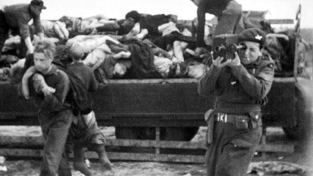 Ein Soldat filmt, während andere Leichen von einem Lastwagen tragen.