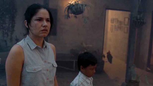 Eine besorgte Frau steht mit einem kleinen Jungen vor einem Haus.