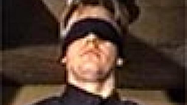 Ein Mann mit verbundenen Augen steht unter einem Holzbalken.