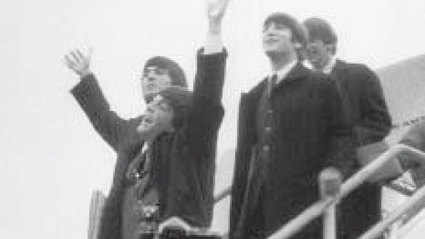 Die Beatles steigen eine Flugzeugtreppe hinunter und winken.