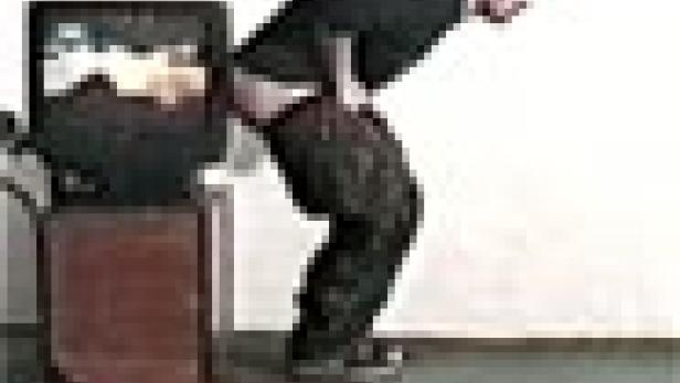 Ein Mann steht auf einem Rollwagen mit einem Fernseher und entblößt sein Gesäß.