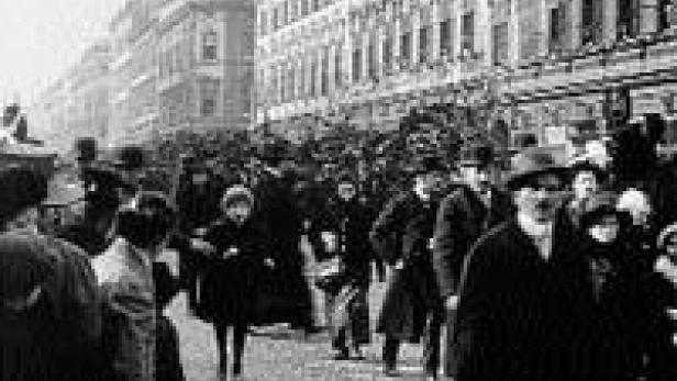 Eine Menschenmenge geht eine belebte Straße entlang, viele tragen Hüte.