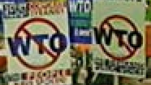 Zwei Schilder mit der Aufschrift „WTO“ und einem durchgestrichenen Kreis werden auf einer Demonstration gezeigt.
