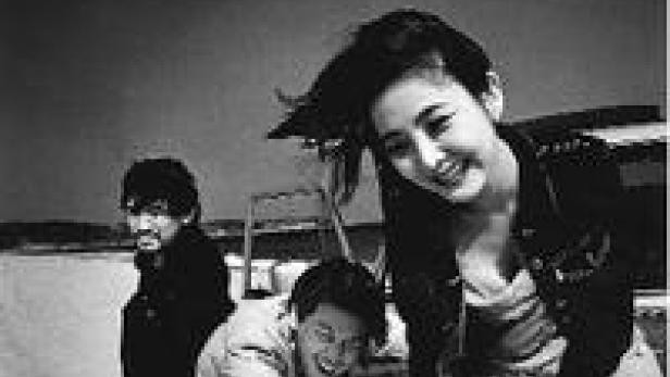 Drei Personen posieren lächelnd für ein Schwarzweißfoto im Freien.