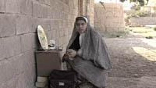 Eine junge Frau kauert neben einer Mauer mit einem kleinen Tisch und einer Tasche.