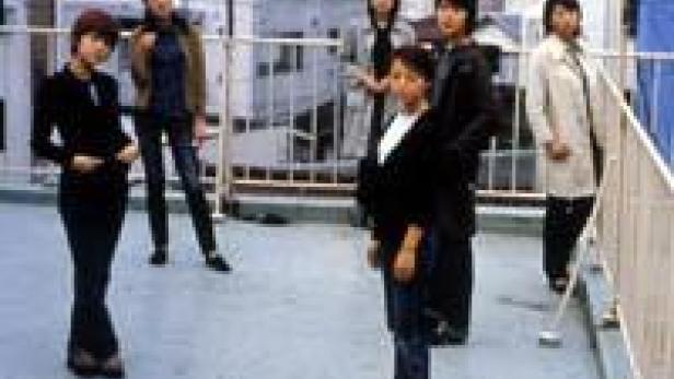 Eine Gruppe von sechs Personen steht auf einer Dachterrasse vor einer Stadtkulisse.