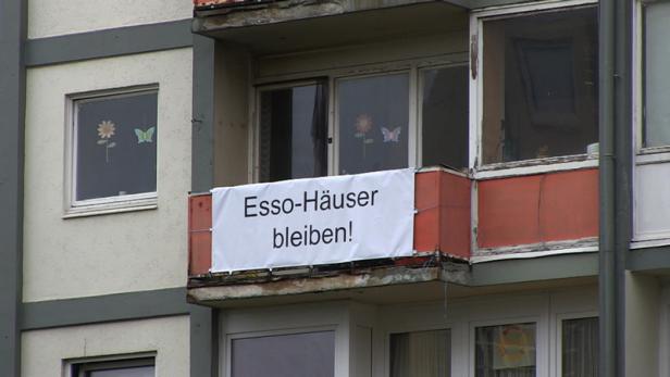 An einem Wohnhaus hängt ein Banner mit der Aufschrift „Esso-Häuser bleiben!“.